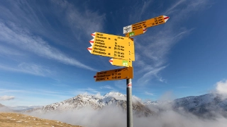 Verschiedene Wegweiser auf einem Wanderweg im Kanton Uri, im Hintergrund die atemberaubende Bergkulisse.